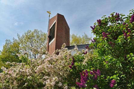 Bloherfelder Kirche. Zu sehen ist der Glockenturm mit bunten Blumen im Vordergrund
